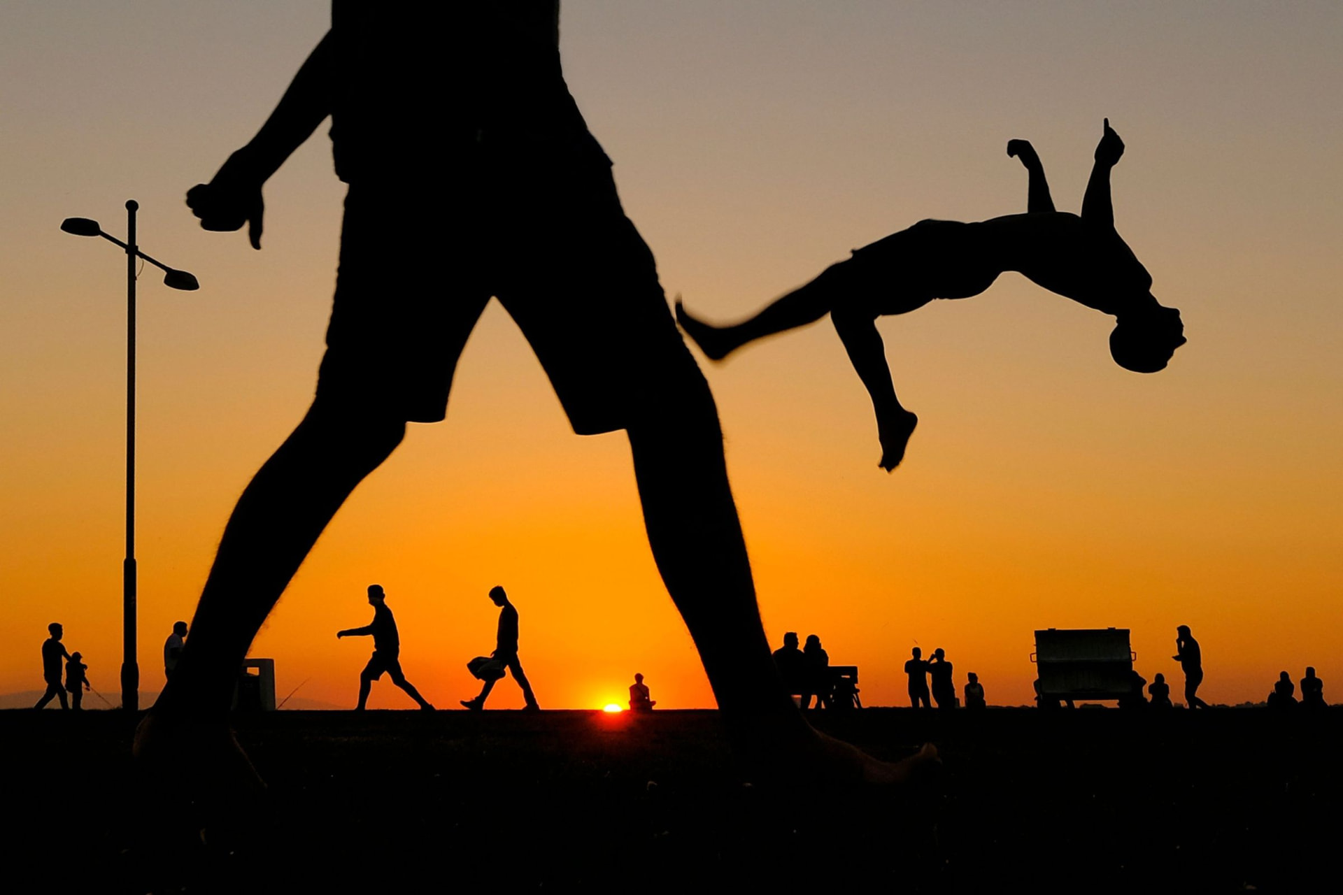 Silhouette di persone al tramonto, una delle quali esegue un salto mortale all'indietro